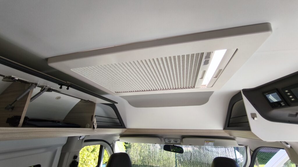 Obrázek interiéru obytného auta, včetně klimatizace a úložných prostor. Elegantní design a funkčnost pro pohodlné cestování.