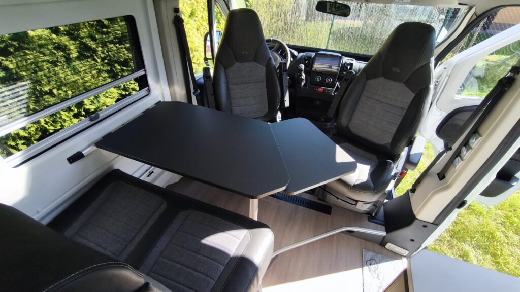 Interiér obytného auta se dvěma sedadly a skládacím stolem. Ideální pro pohodlné cestování a odpočinek.