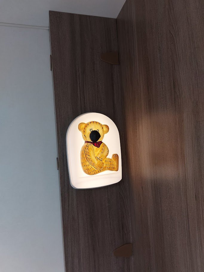 Obrázek ukazuje svítidlo ve tvaru medvídka v interiéru. Není to obytné auto ani karavan.