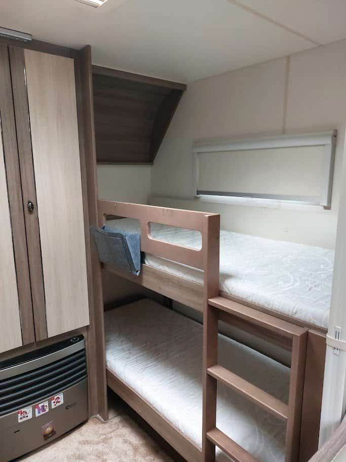 Obrázek ukazuje interiér karavanu s patrovými postelemi a úložným prostorem. Ideální pro rodinné výlety.