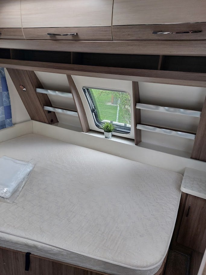 Interiér karavanu s pohodlnou postelí a úložnými prostory. Ideální pro vaše cestování a odpočinek.