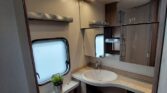 Obrázek zobrazuje moderní koupelnu v karavanu s umyvadlem, sprchou a toaletou. Elegantní design a praktické uspořádání.