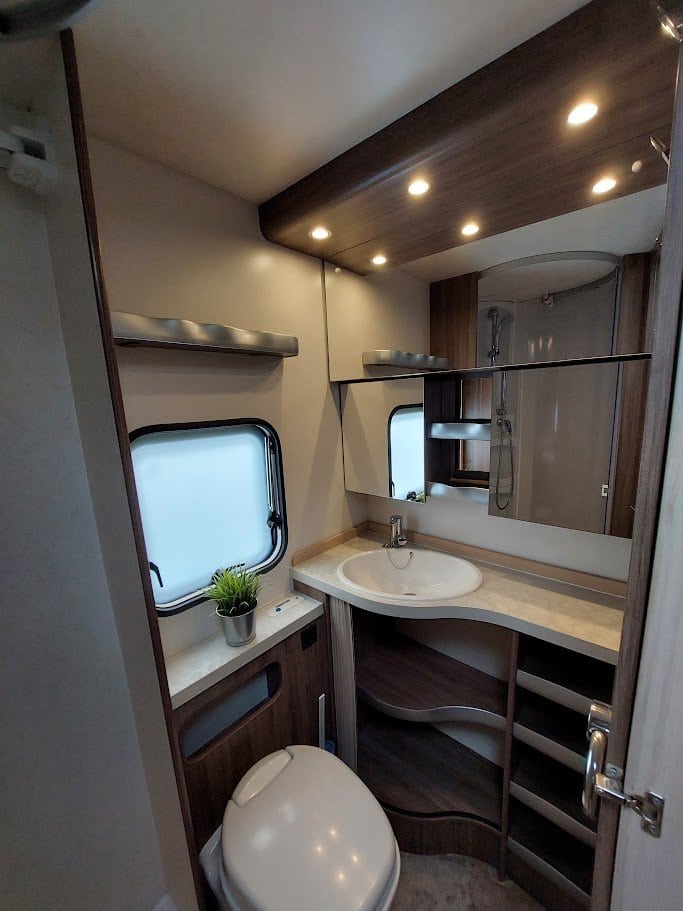 Obrázek zobrazuje moderní koupelnu v karavanu s umyvadlem, sprchou a toaletou. Elegantní design a praktické uspořádání.