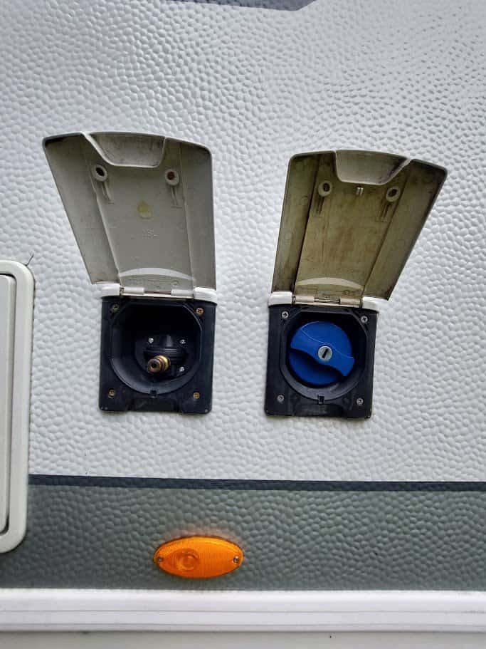 Na obrázku jsou připojovací porty karavanu pro vodu a elektriku. Ideální pro pohodlné cestování.