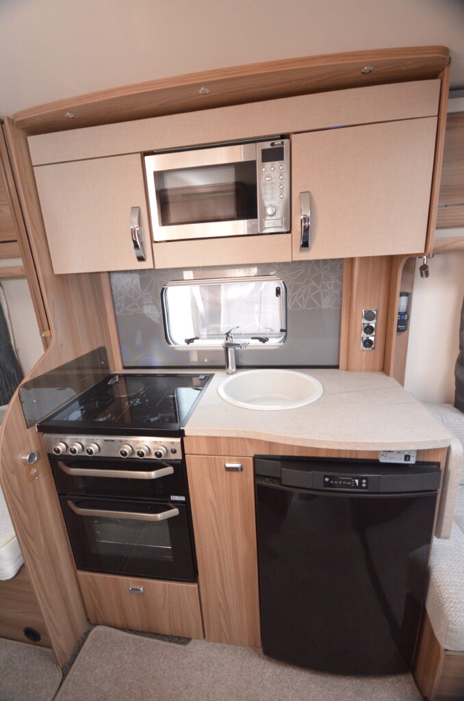 Obrázek interiéru moderního obytného auta s kuchyňským koutem, sporákem a mikrovlnnou troubou.