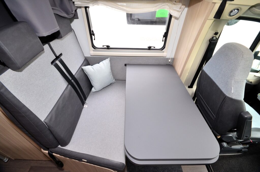 Interiér obytného auta s pohodlnou sedačkou, stolem a světlem. Ideální pro relaxaci a odpočinek na cestách.