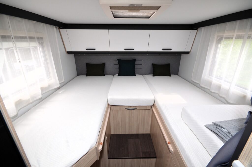 Obrázek interiéru obytného auta s prostornými lůžky a moderním designem, ideální pro pohodlné cestování.