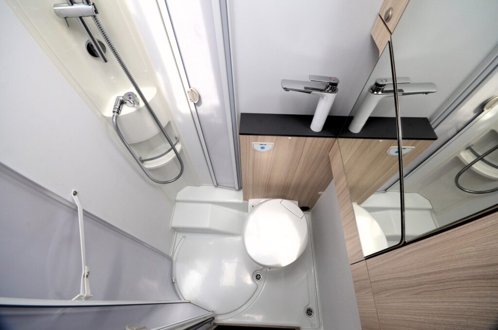Koupelna s toaletou a sprchovým koutem v obytném voze, moderní design a praktické uspořádání.