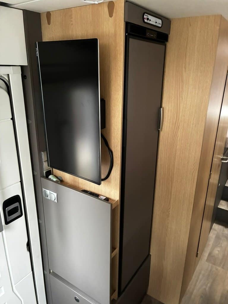 Obrázek interiéru obytného vozu s televizí a lednicí. Moderní design a funkční uspořádání pro komfortní cestování.