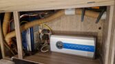 Na fotografii je část interiéru karavanu s elektrickými komponenty a hadicemi. Značka přístroje není viditelná.