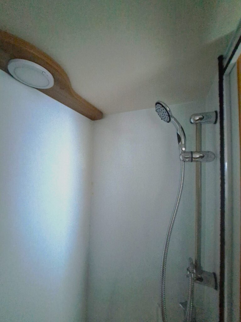 Obrázek ukazuje sprchu v obytném voze. Design je moderní a minimalistický, ideální pro kempování.