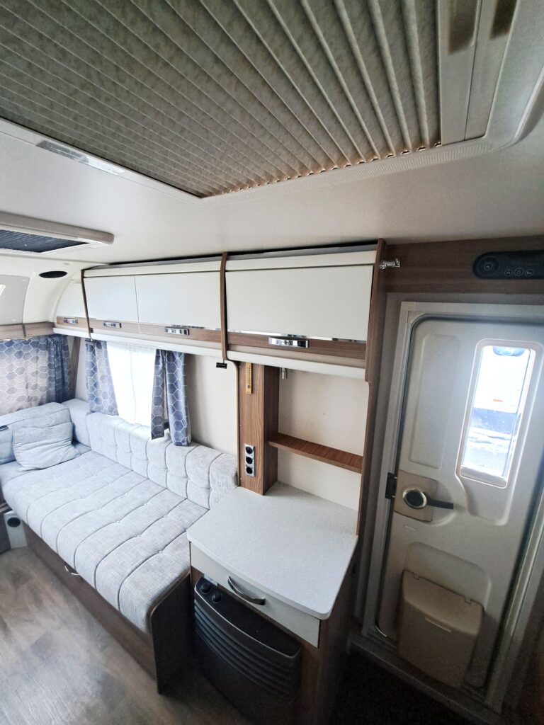 Obrázek interiéru karavanu s pohodlným gaučem a moderním vybavením. Ideální pro cestování a odpočinek.