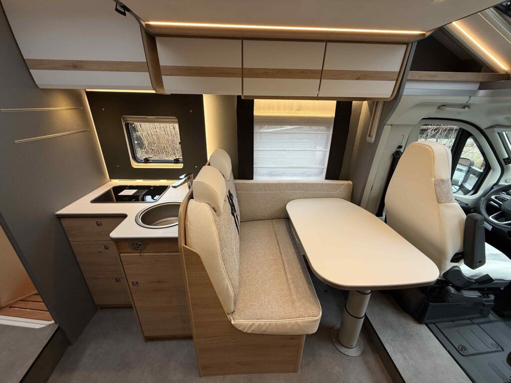 Interiér obytného auta s moderním designem, kuchyňskou linkou a pohodlným sezením. Značka a model nejsou viditelné.