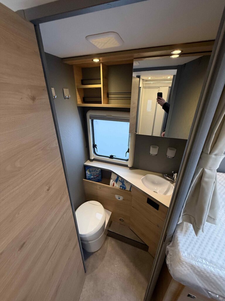 Obrázek interiéru karavanu s moderním designem, toaletou a umyvadlem. Ideální pro pohodlné cestování.