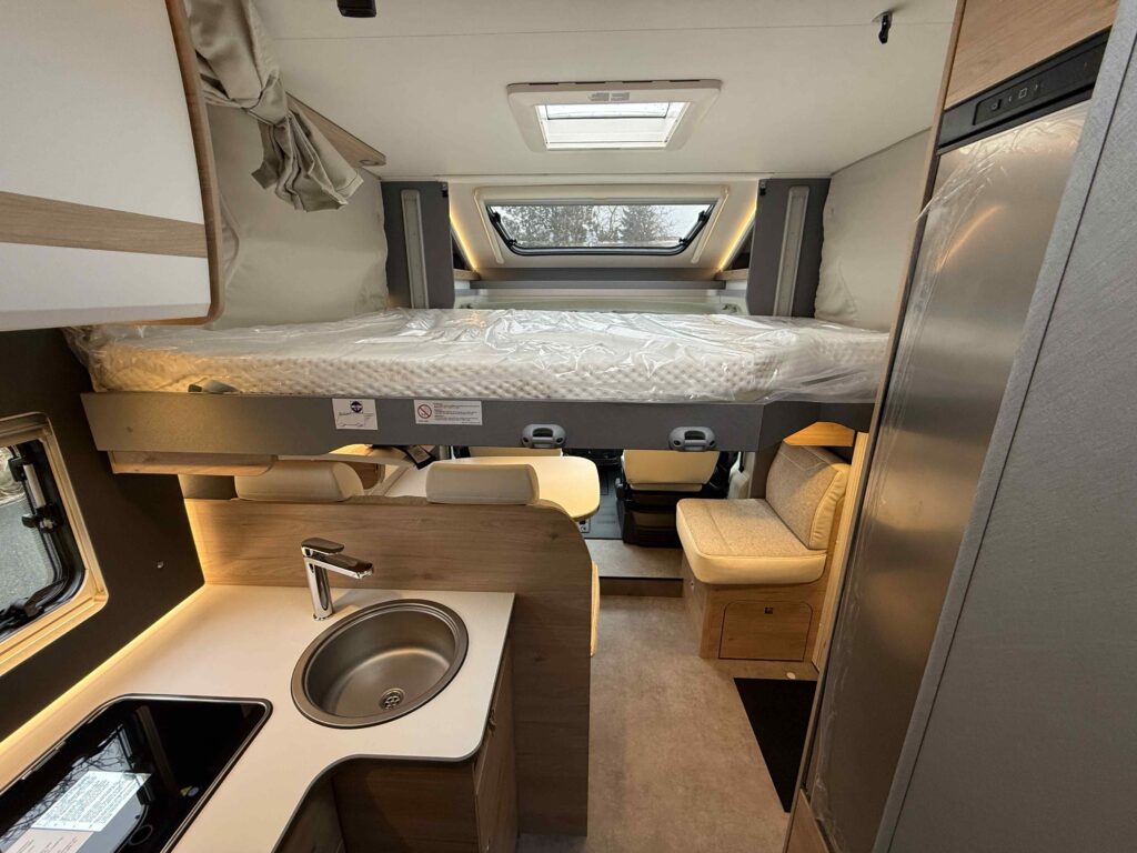 Moderní obytné auto s praktickým interiérem a lůžkem nad kuchyňskou linkou. Ideální pro pohodové cestování.