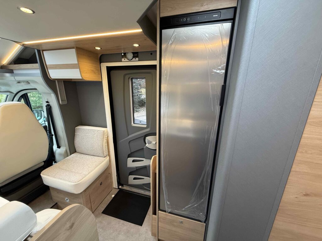 Moderní interiér obytného auta s pohodlným sezením a vestavěnými spotřebiči, ideální pro cestování a kempování.
