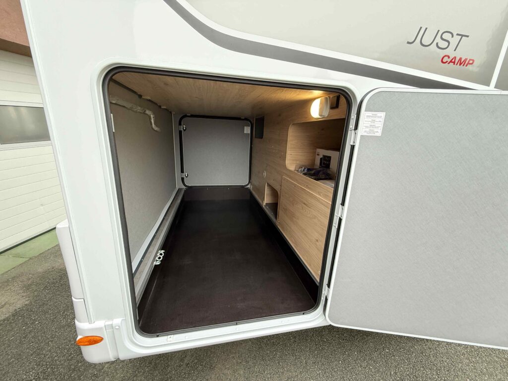 Obrázek zobrazuje interiér karavanu JUST CAMP s prostorným úložným prostorem a dřevěnými prvky.