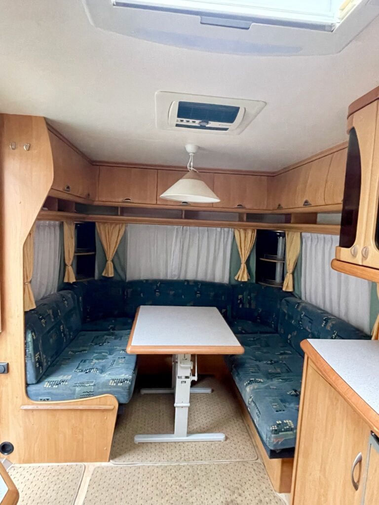 Interiér karavanu, pohodlné sezení a jídelní stůl pro příjemné chvíle na cestách. Ideální pro rodinné výlety.