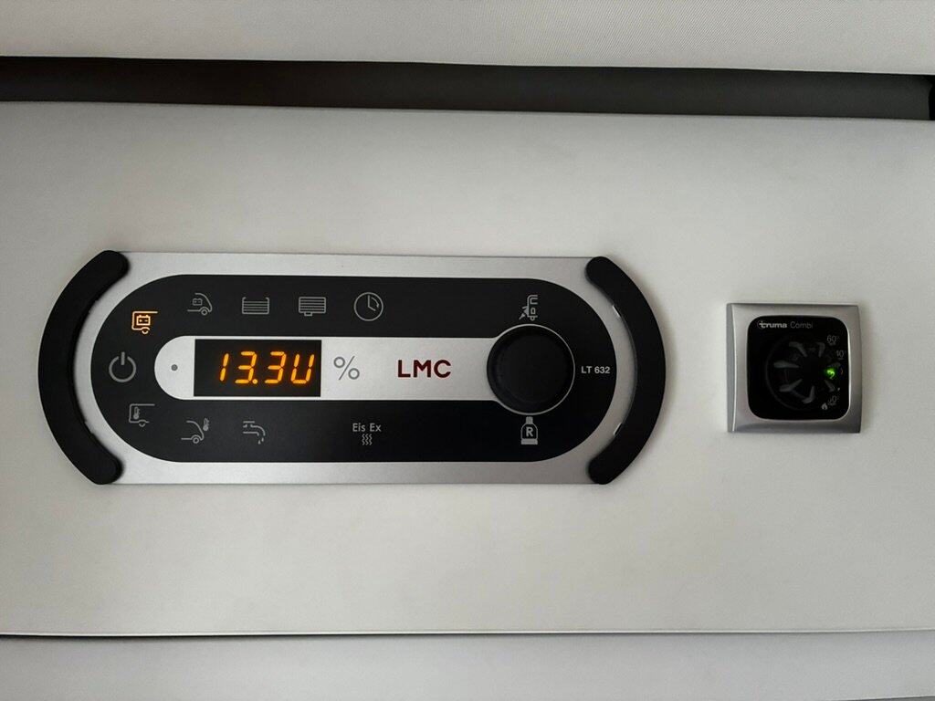 Obrázek ukazuje ovládací panel obytného auta značky LMC s informacemi o baterii a topení.