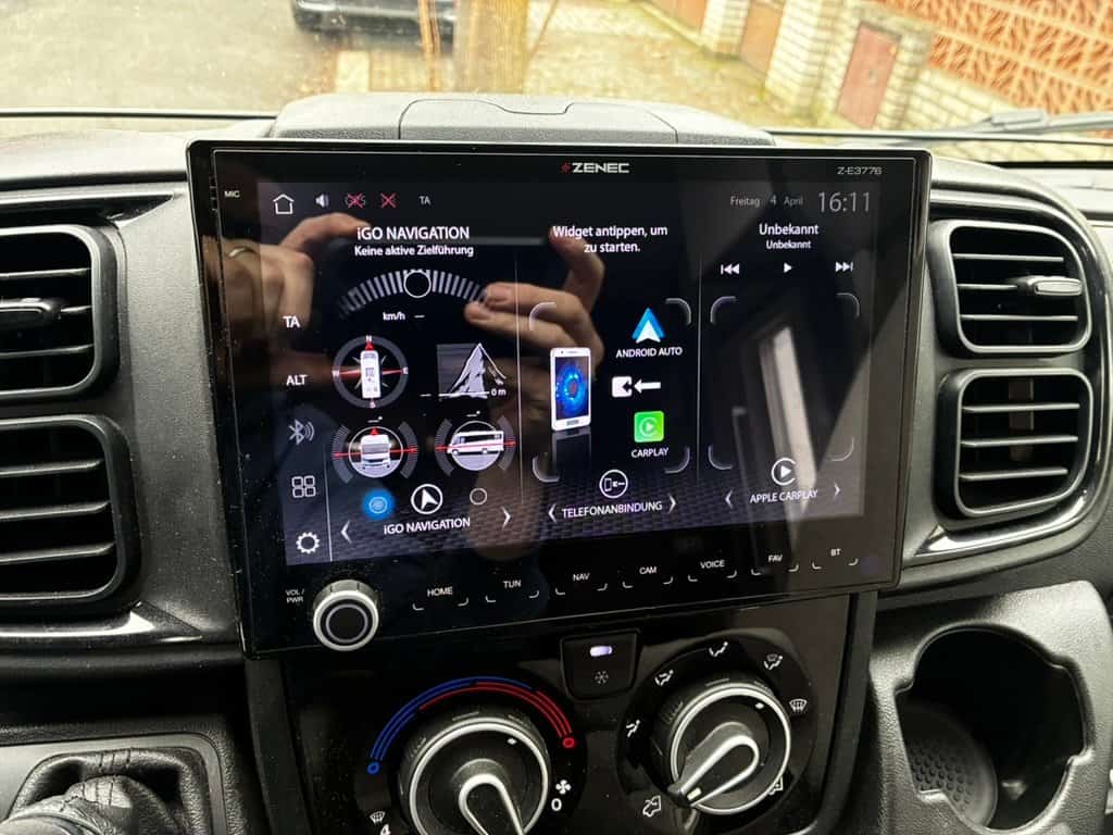 Obrázek zobrazuje moderní palubní displej obytného auta s navigací a multimediálními funkcemi.