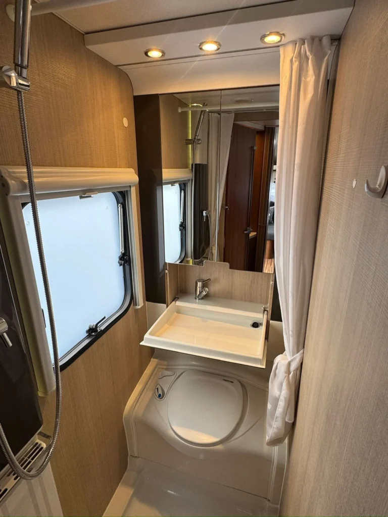 Obrázek koupelny v obytném autě, moderní design s umyvadlem a sprchou. Komfortní a stylové uspořádání.