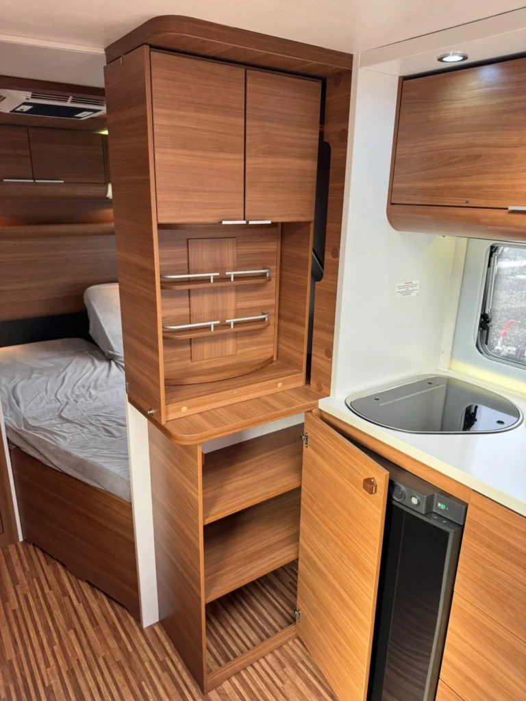 Interiér obytného auta s dřevěným nábytkem a moderními spotřebiči. Ideal pro komfortní cestování.