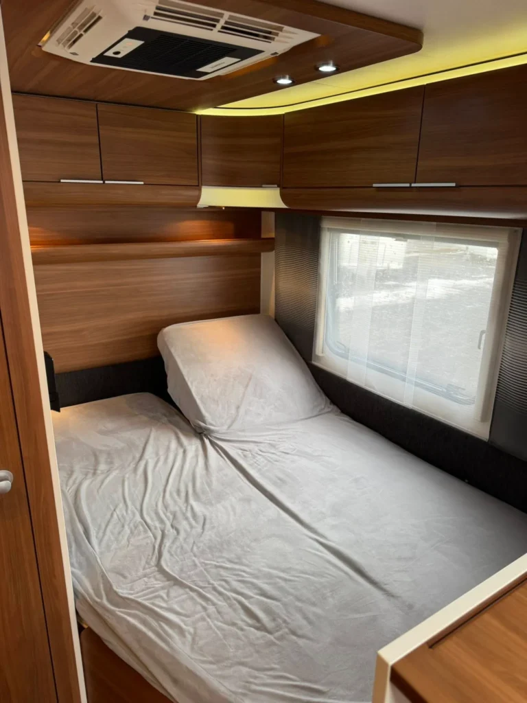 Interiér obytného vozu s pohodlnou postelí a úložnými prostory. Ideální pro relaxaci na cestách.