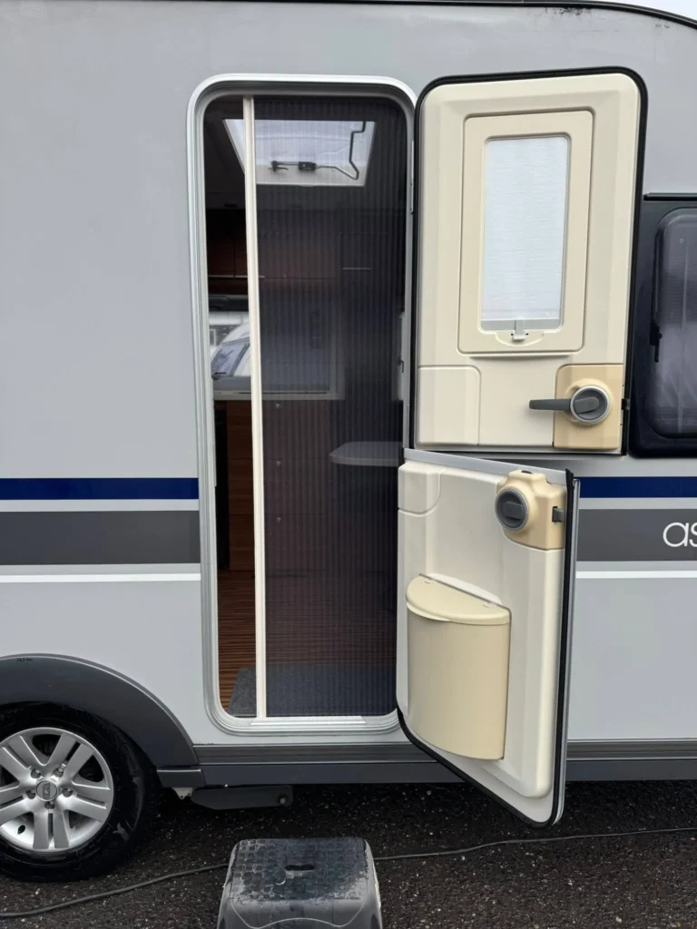 Obrázek zobrazuje karavan Ascaris s bočními dveřmi a výhledem na interiér. Ideální pro pohodlné cestování!