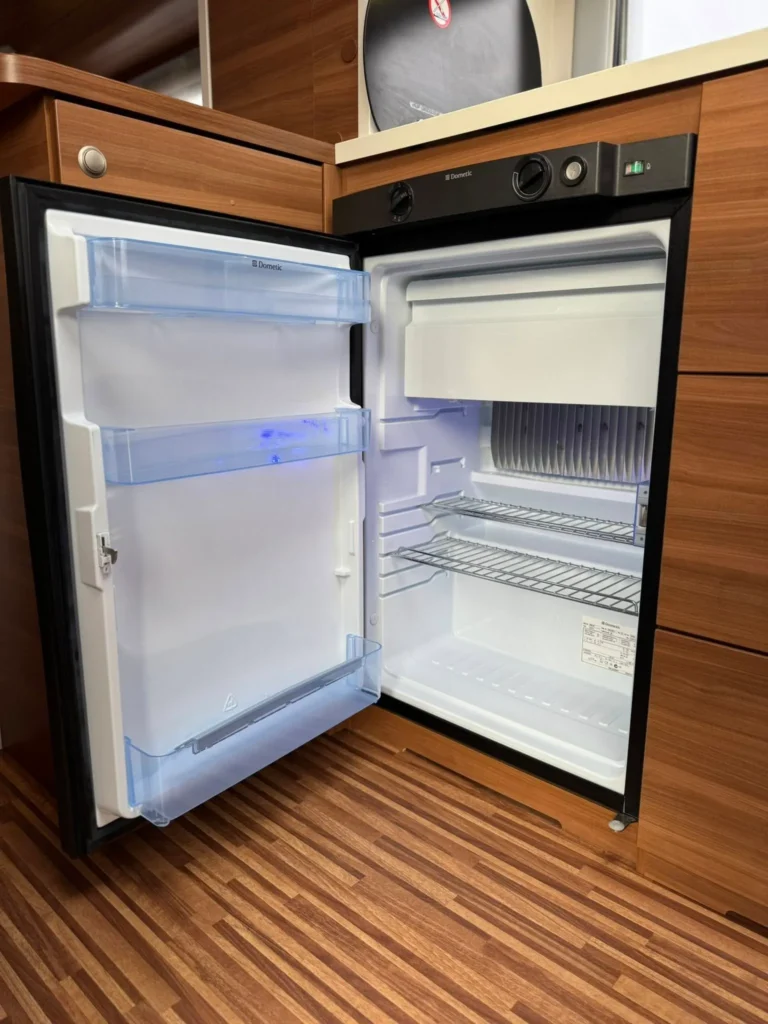 Obrázek ukazuje lednici značky Dometic uvnitř obytného vozu, ideální pro kempování. Kvalitní zařízení pro uchování potravin.