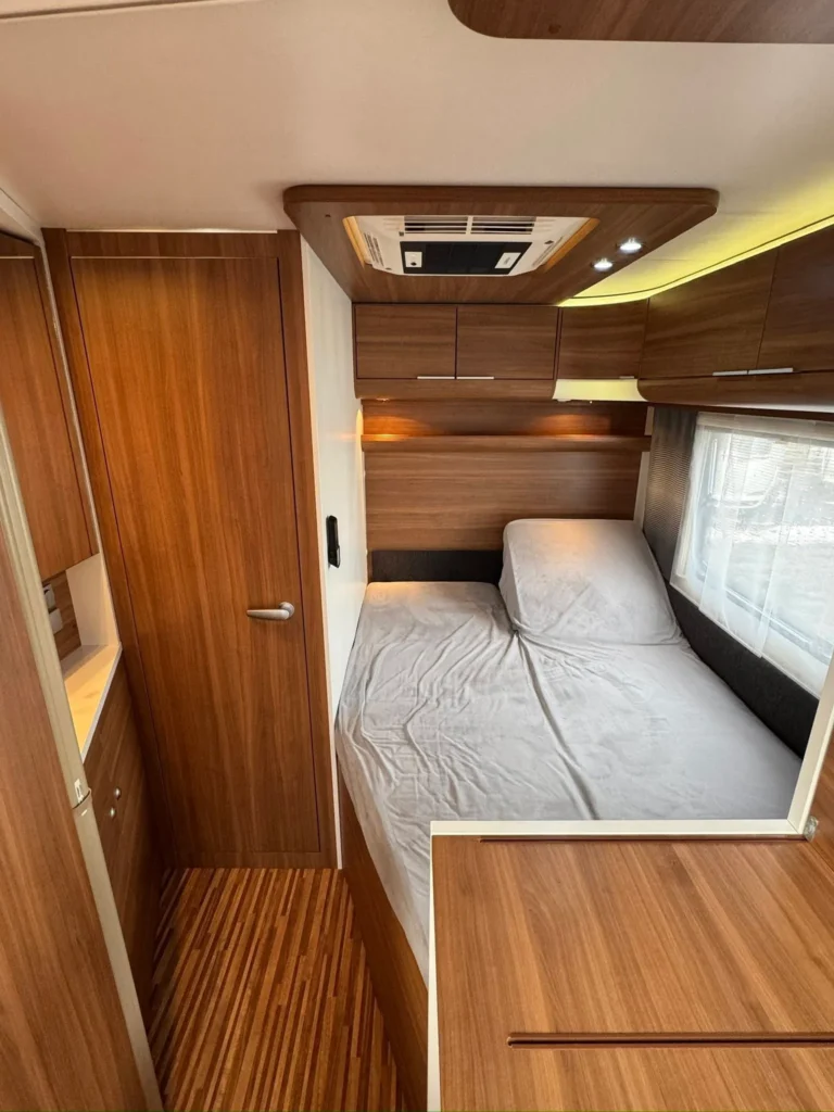 Interiér karavanu s dřevěnými prvky a pohodlnou postelí. Ideální pro kempování a odpočinek na cestách.