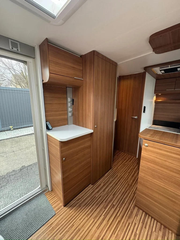 Interiér karavanu s dřevěným nábytkem a moderním designem. Vidět kuchyňský kout a úložné skříňky.