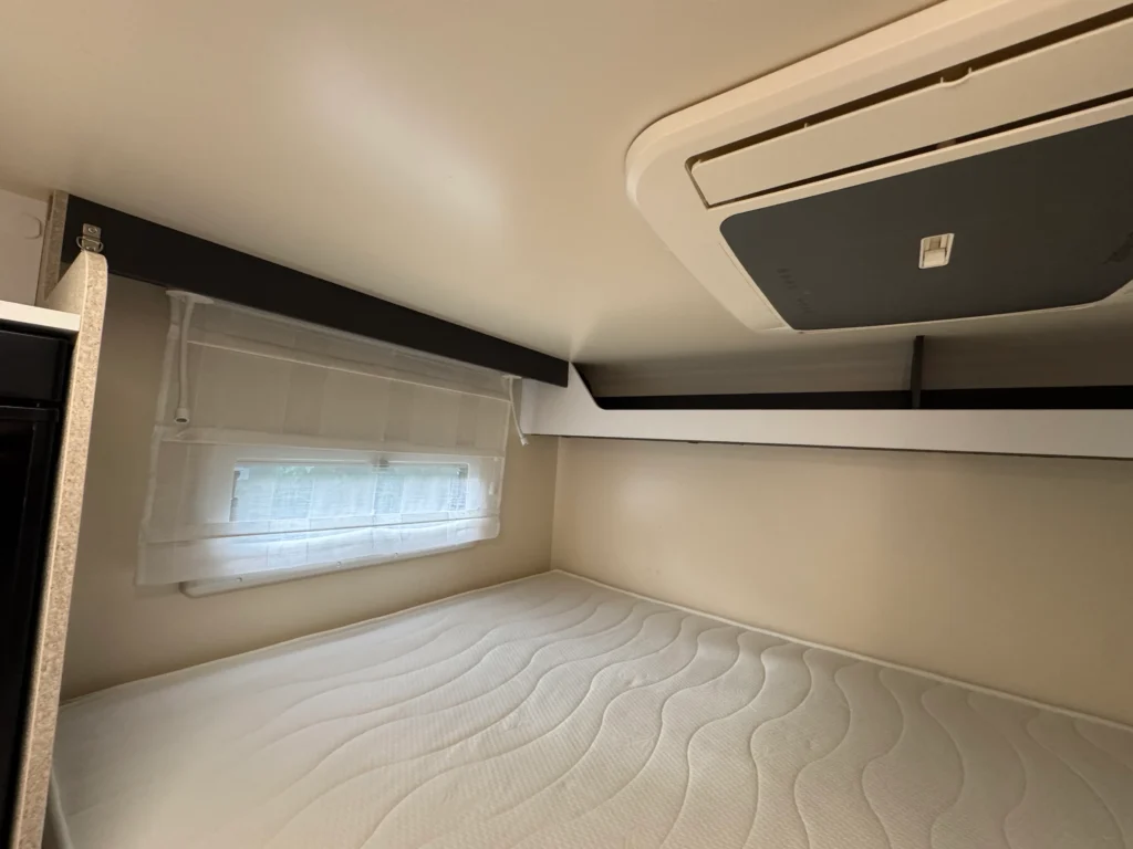 Obrázek interiéru karavanu s pohodlnou postelí a oknem, které zajišťuje dostatek přirozeného světla.
