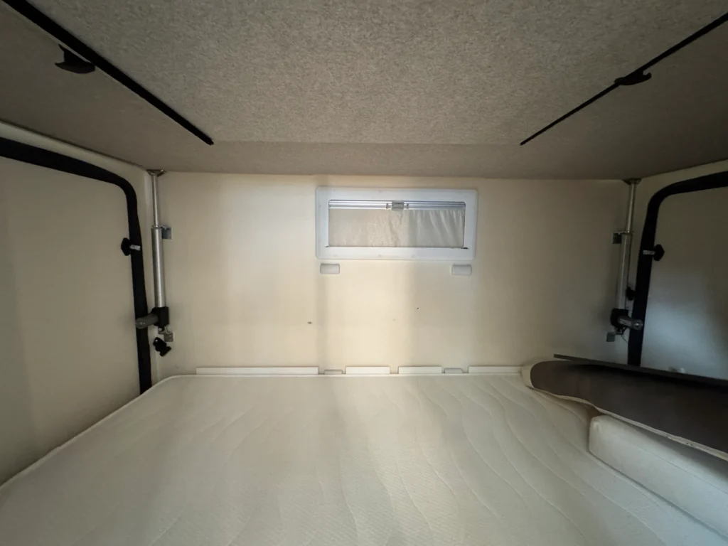 Interiér karavanu s postelí a oknem pro přirozené osvětlení, ideální pro kempaření a odpočinek na cestách.