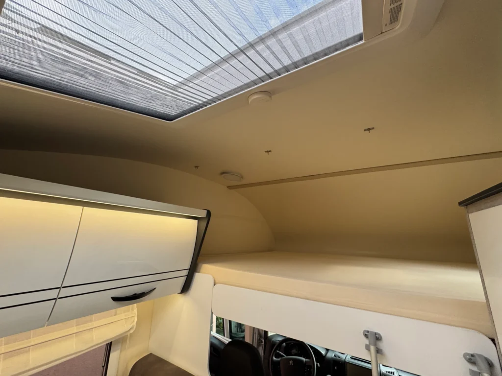 Interiér obytného auta s úložným prostorem a panoramatickým střešním oknem. Moderní a prostorný design.