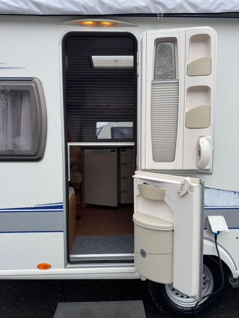 Obrázek zobrazuje karavan s otevřenými dveřmi, nabízí útulný interiér a praktické funkce.