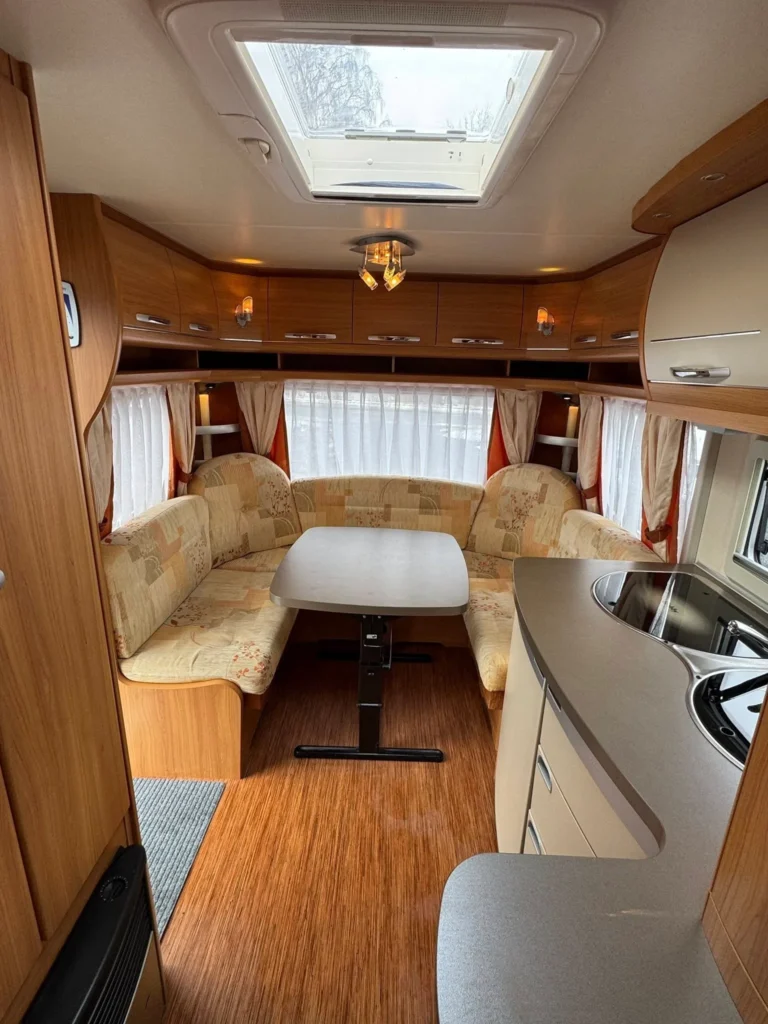 Interiér karavanu s jídelním koutem a kuchyňským pultem, ideální pro pohodlné cestování.