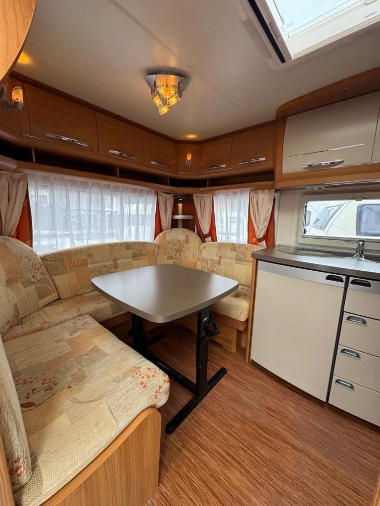 Obrázek interiéru karavanu s pohodlným posezením a kuchyňským koutem. Ideální pro rodinné cestování.