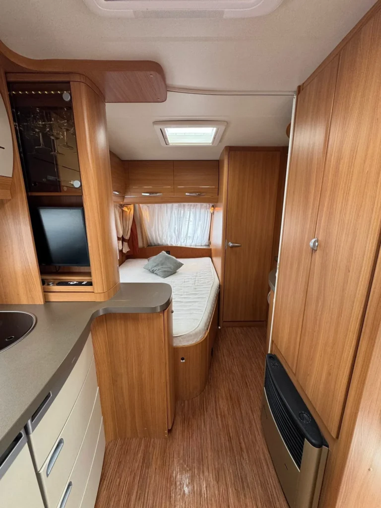 Interiér karavanu s dřevěnými akcenty, pohodlným lůžkem a kuchyňským koutem. Ideální pro dovolenou na cestách.