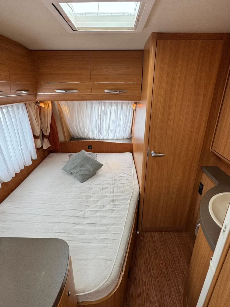 Interiér karavanu s dřevěným obložením, pohodlnou postelí a kuchyňským koutem. Ideální pro pohodové cestování.