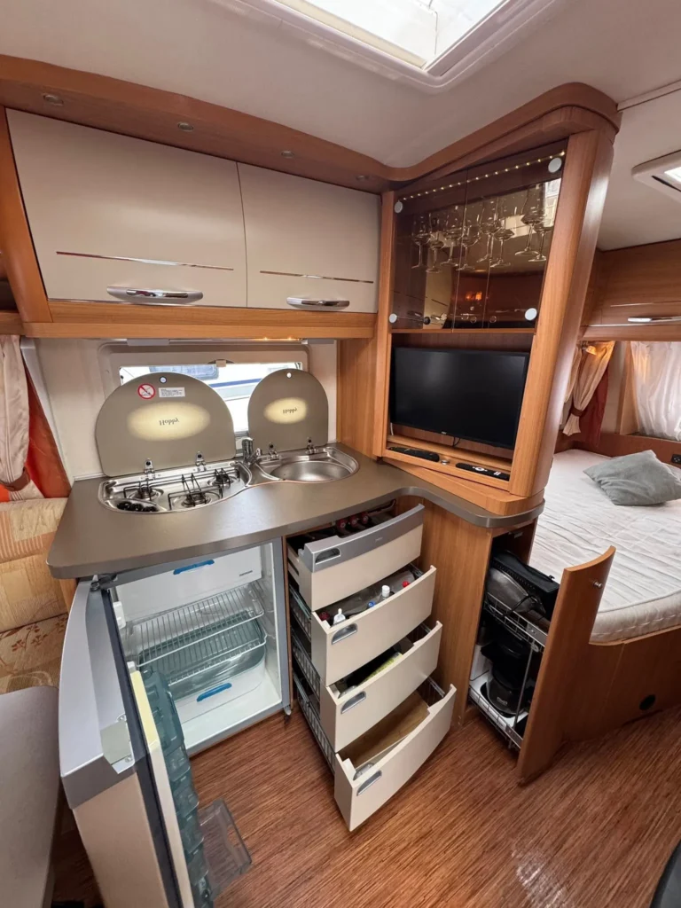 Interiér obytného auta s kuchyňskou linkou, varnou deskou a ledničkou. Ideální pro pohodlné cestování.