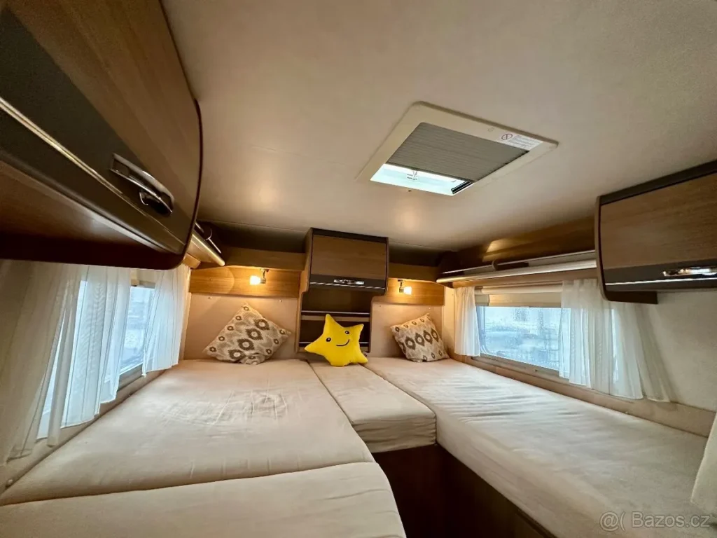 Pohodlný interiér karavanu s útulnými postelemi a úložným prostorem. Ideální pro odpočinek na cestách.