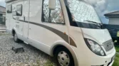 Obytné auto Hymer E 654 na slunném pozemku, ideální pro dobrodružství na cestách.