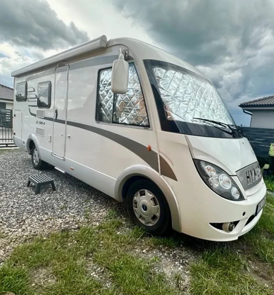 Obytné auto Hymer E 654 na slunném pozemku, ideální pro dobrodružství na cestách.