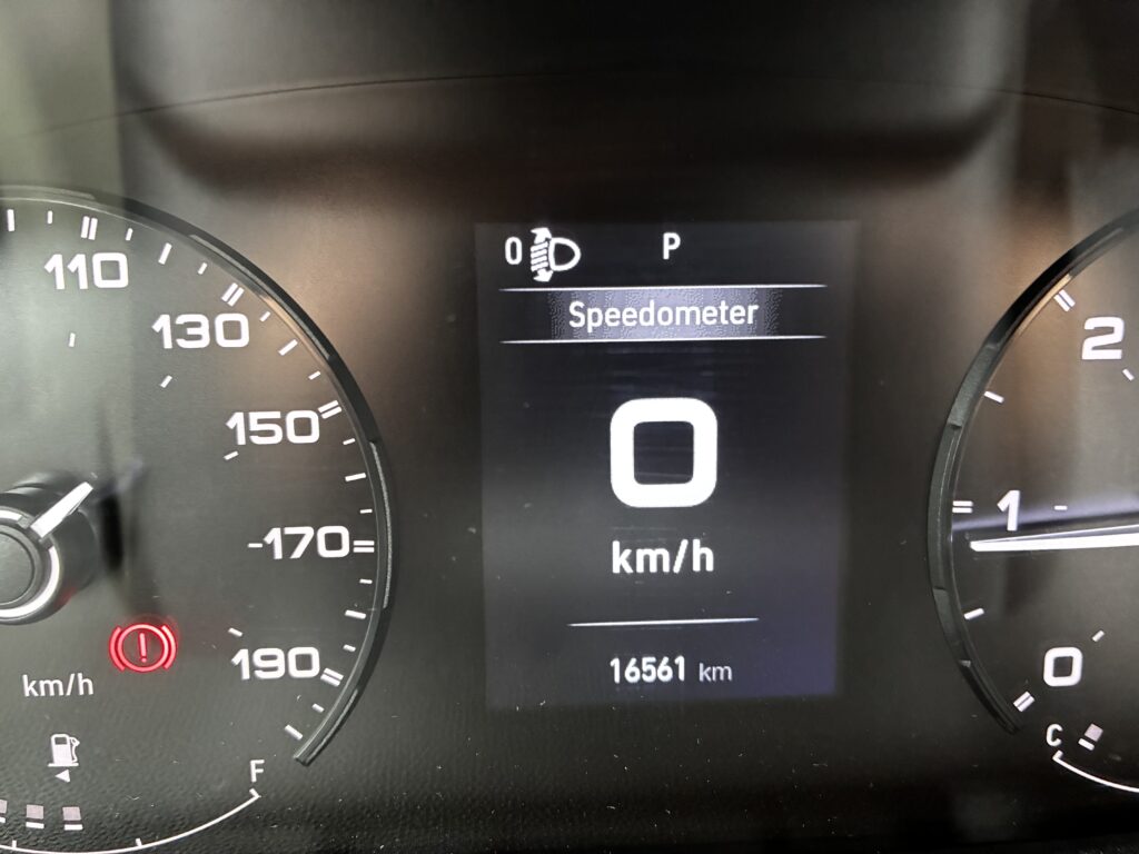 Obrázek ukazuje přístrojovou desku vozidla se speedometrem na 0 km/h a celkovým počtem kilometrů 16 561.