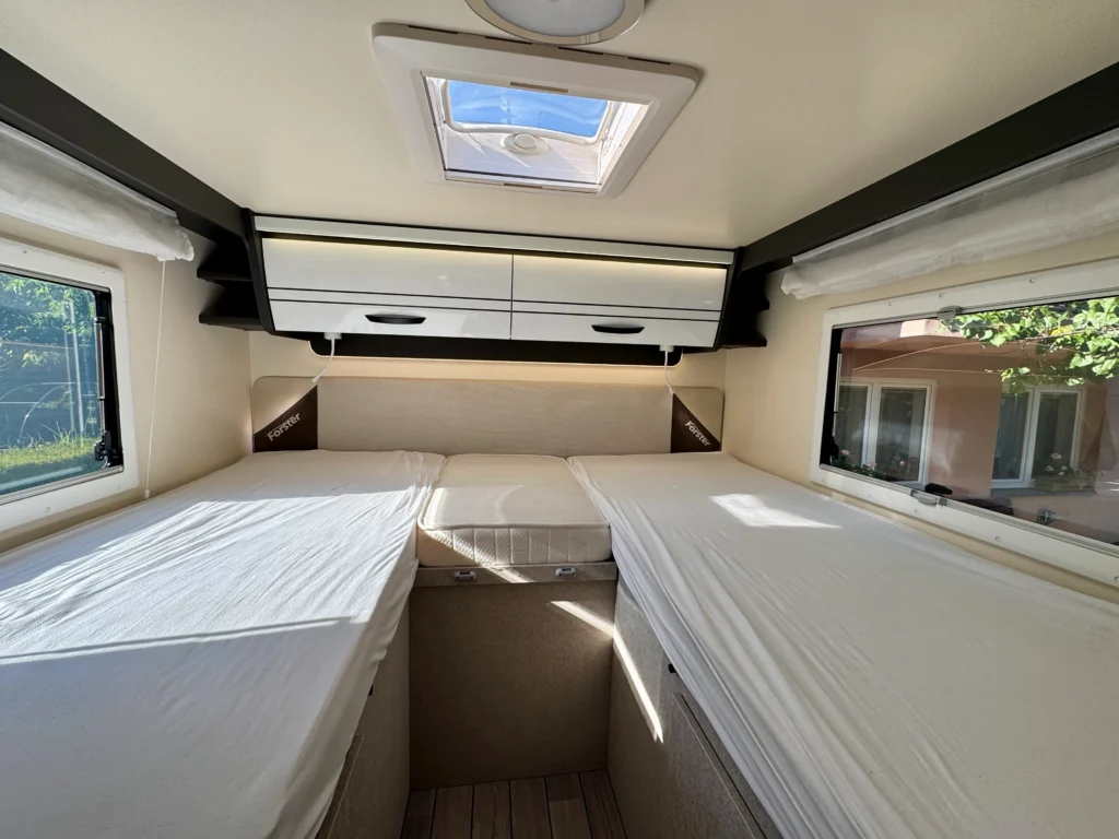 Interiér obytného auta Forster. Dvě lůžka, dostatek úložného prostoru a přirozené osvětlení. Ideální pro cestovatele.