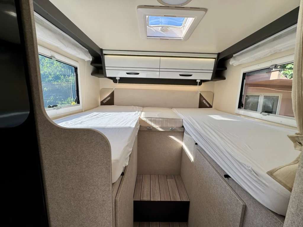 Interiér karavanu Forster s dvěma lůžky a úložným prostorem. Moderní a světlý design pro pohodlné cestování.