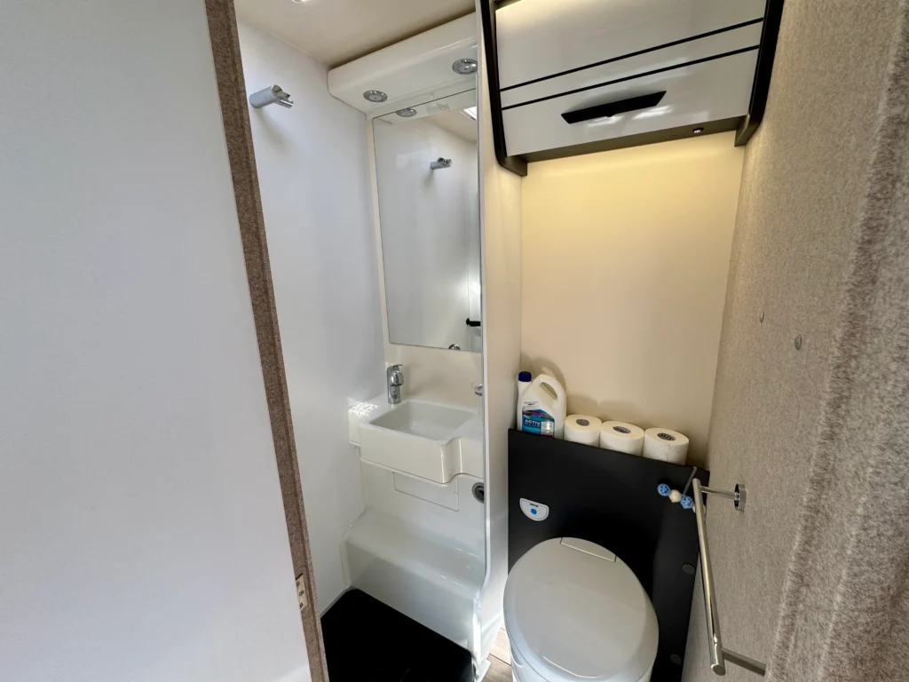Obrázek zobrazuje moderní koupelnu v obytném autě s umyvadlem a toaletou. Komfortní vybavení pro cestování.