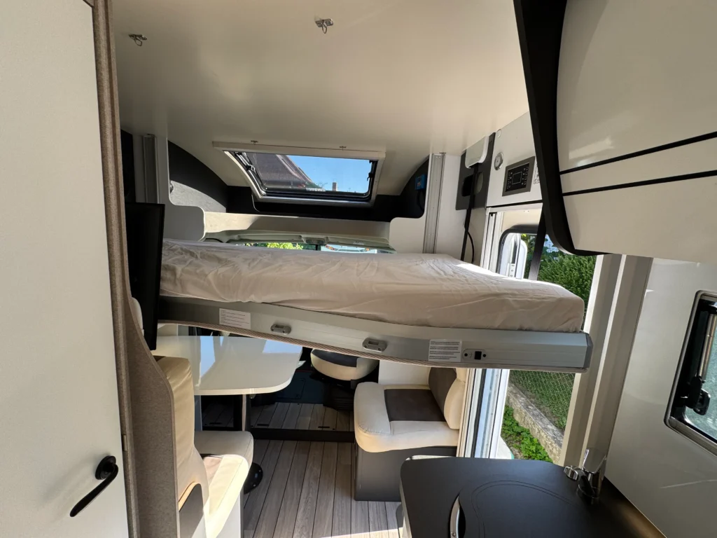Interiér moderního obytného auta s rozkládací postelí a stylovým posezením.