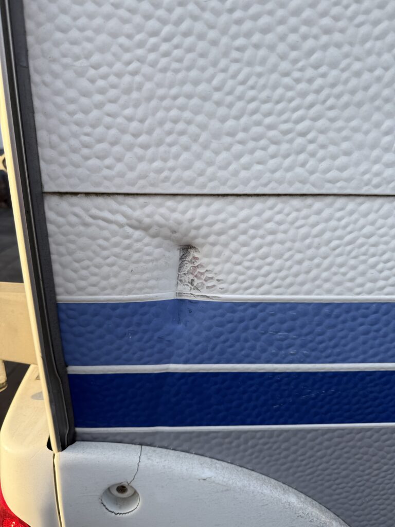 Na obrázku je poškození karavanu, detail zdi s promáčknutím a prasklinou.