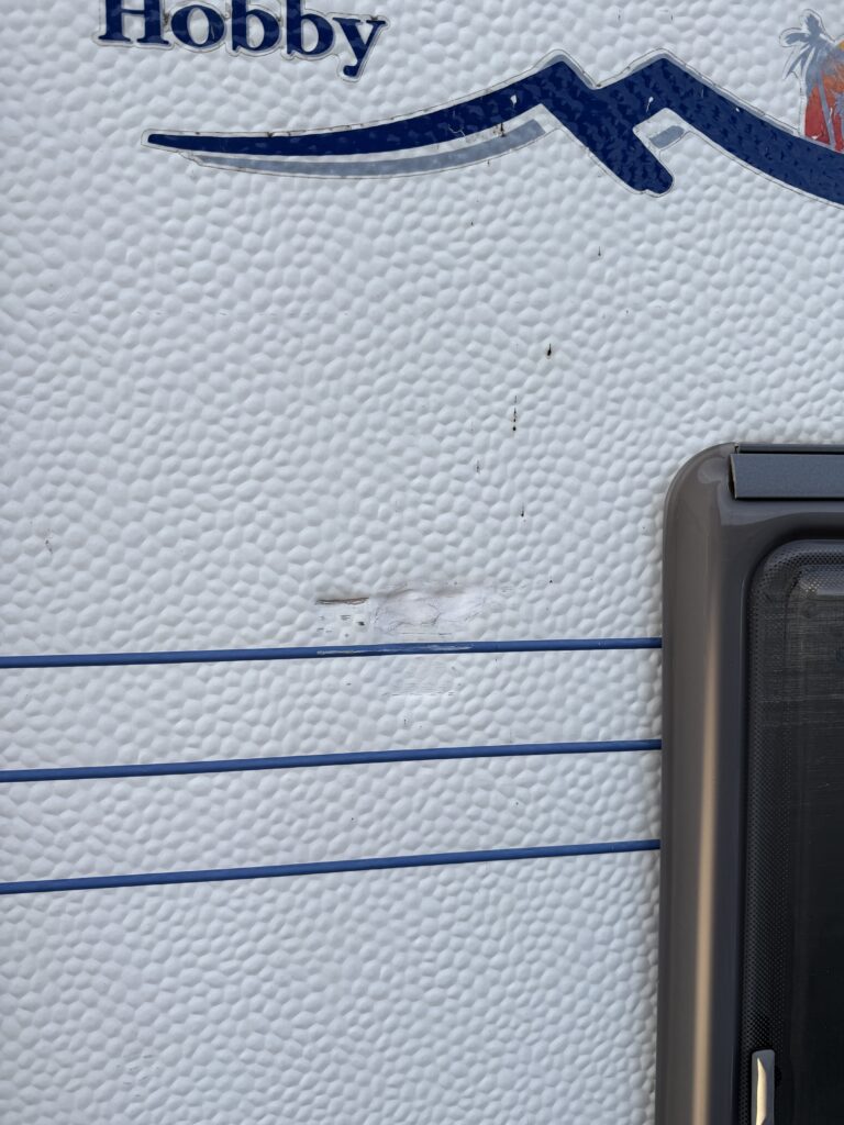 Na obrázku je karavan značky Hobby se drobnými oděrkami na povrchu. Ideální pro cestování a dovolenou.